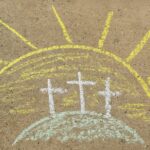 Sidewalk chalk drawing of three crosses on a hill with a bright sun in the background, symbolizing the resurrection of Jesus Christ on Easter morning.