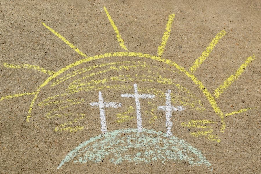 Sidewalk chalk drawing of three crosses on a hill with a bright sun in the background, symbolizing the resurrection of Jesus Christ on Easter morning.