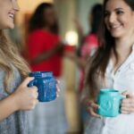 Two women smiling and holding coffee mugs while enjoying conversation, symbolizing friendship, trust, and the importance of believing the best in others.